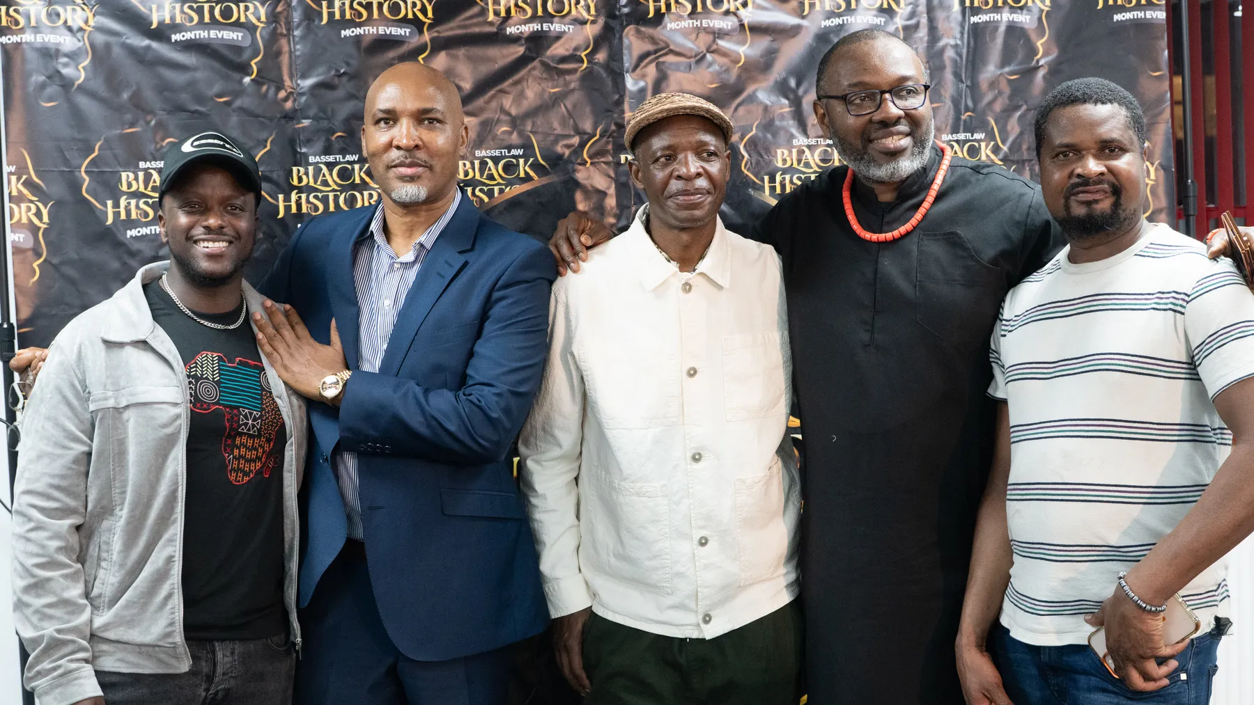 Five men gathered in front of a Black History Month backdrop.