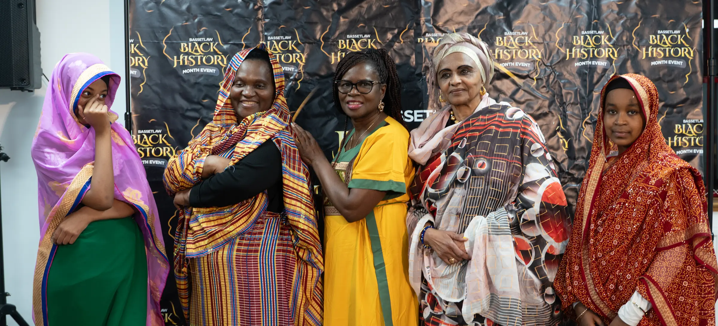 Five women in colourful outfits standing together at a Black History Month gathering.