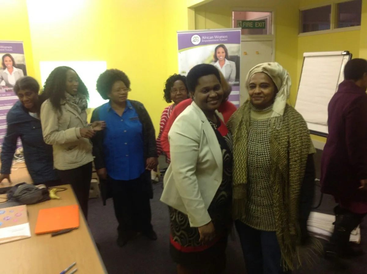 Women greeting each other at an AWEF community session, with AWEF banners behind them.