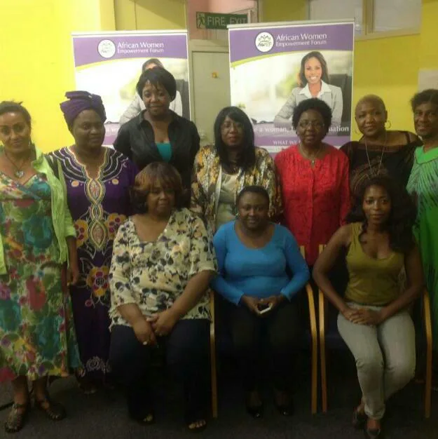 Women seated and standing together in front of AWEF banners at a community session in 2015.