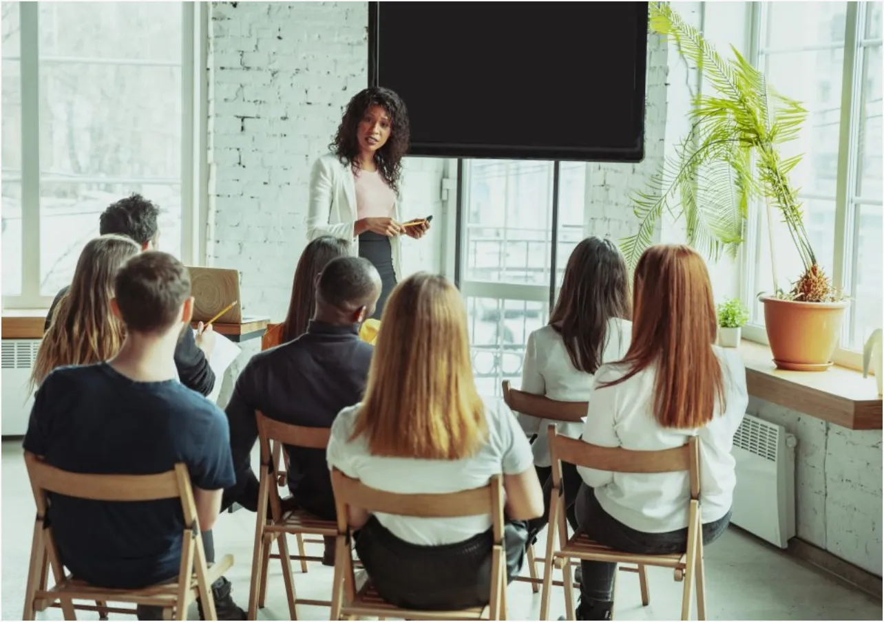 A trainer presenting to a seated group in a bright room.