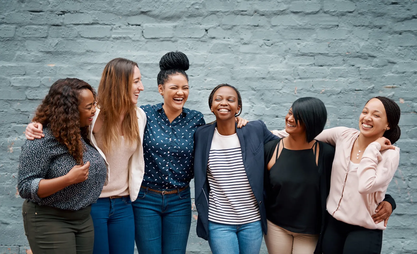 A group of women laughing together against a brick wall.