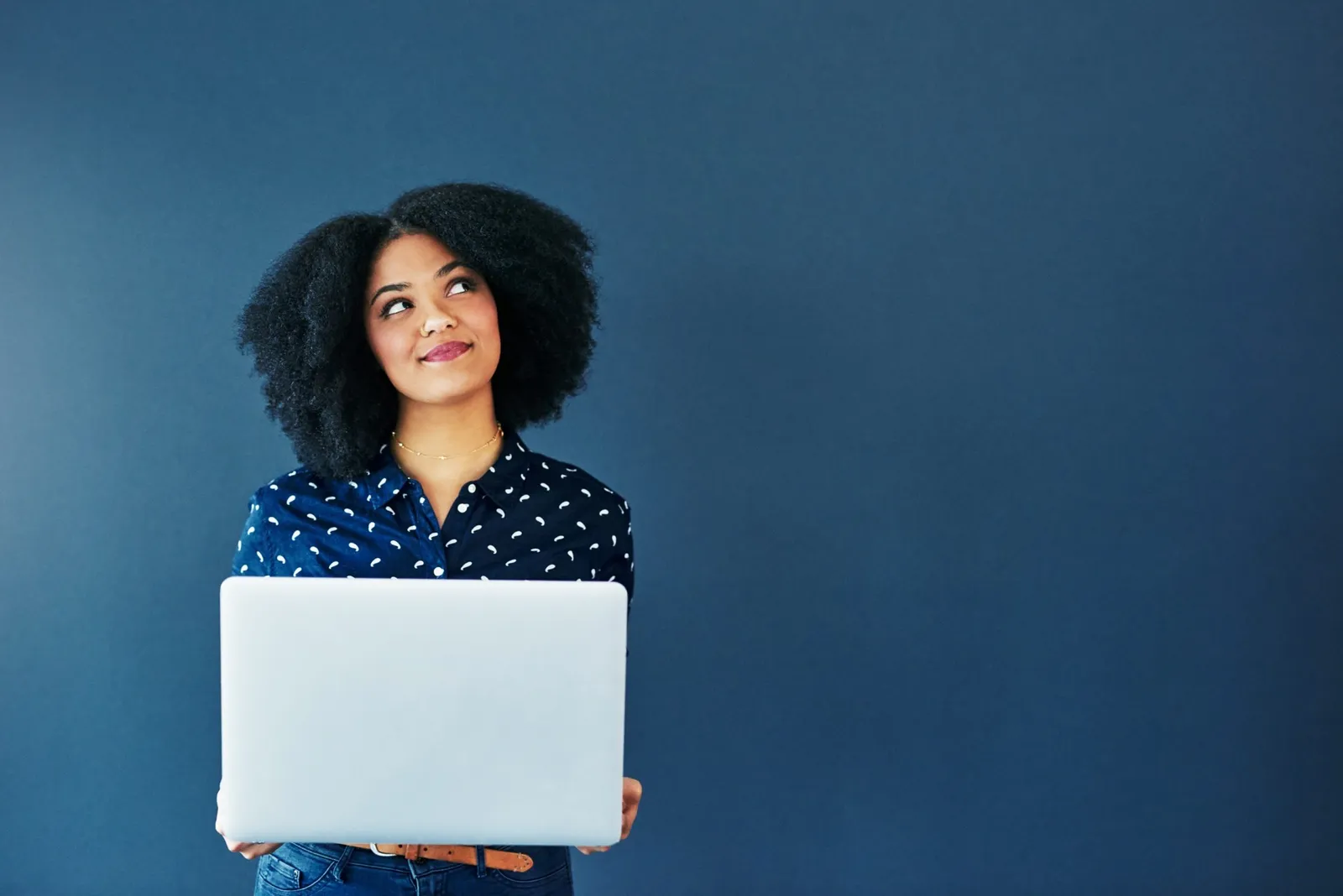 A woman holding a laptop and looking up thoughtfully.