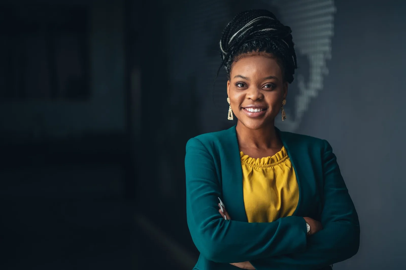 A woman in a teal jacket smiling with her arms folded.