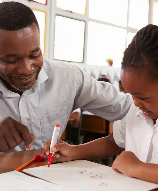 teacher-helping-elementary-school-girl-at-her-desk-P56F9ZG_1